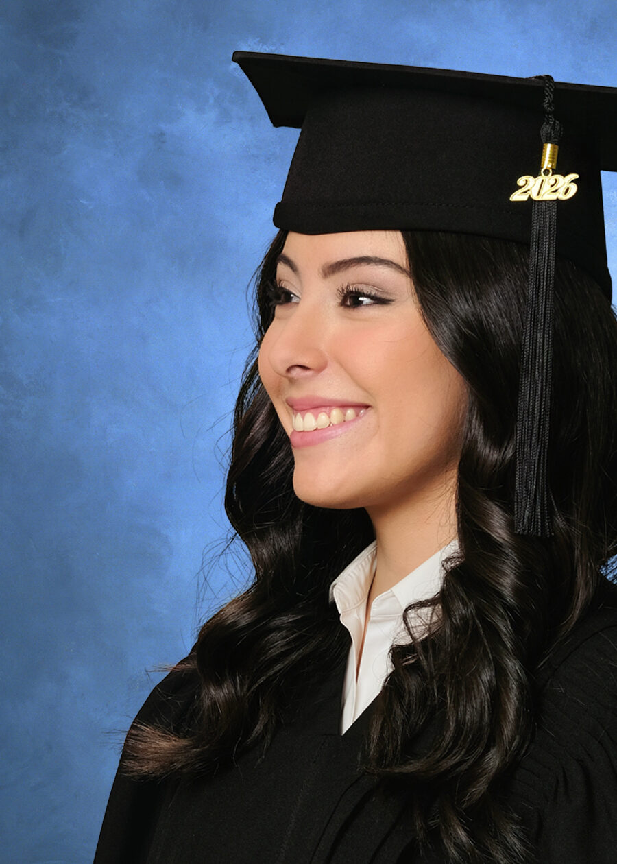GradPase_Look A close-up high school graduation portrait of a girl wearing a cap and gown against a traditional blue background. This pose is from Studio NanC's Supreme graduation session.